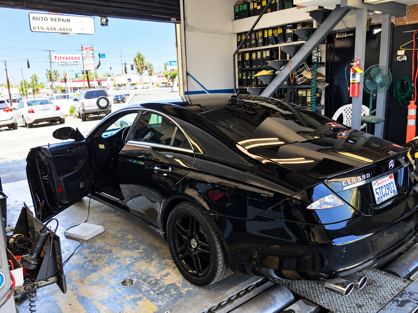 Black sports coupe at a gas station bay with its driver door open and trunk area exposed