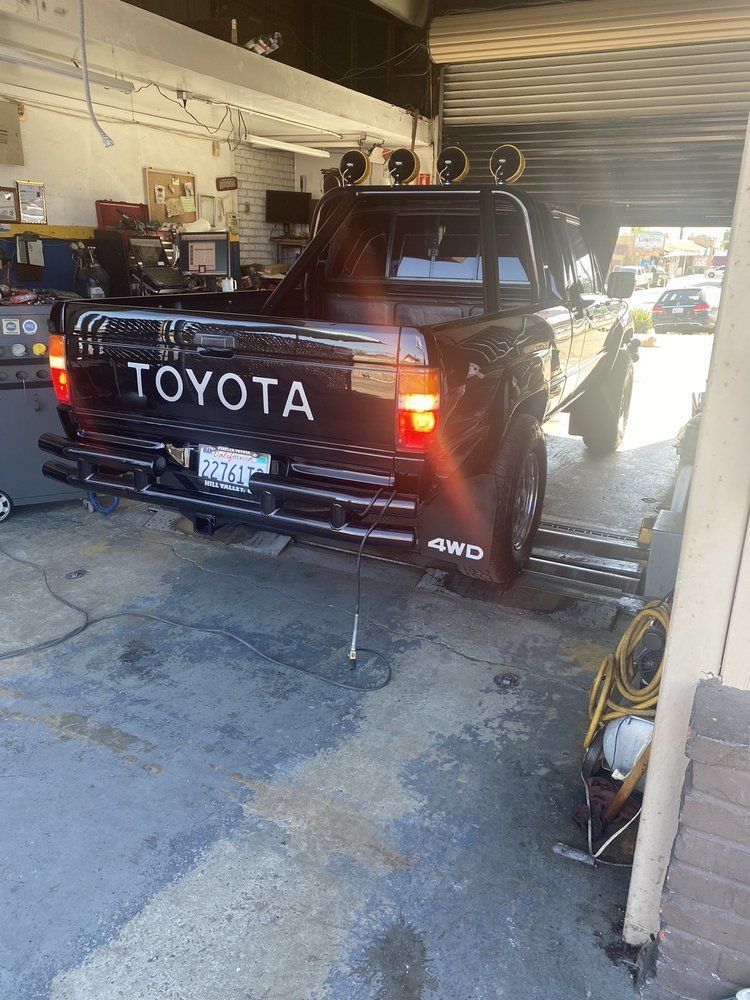 Black Toyota pickup in a garage, rear view with tailgate open and bright sunlight outside.