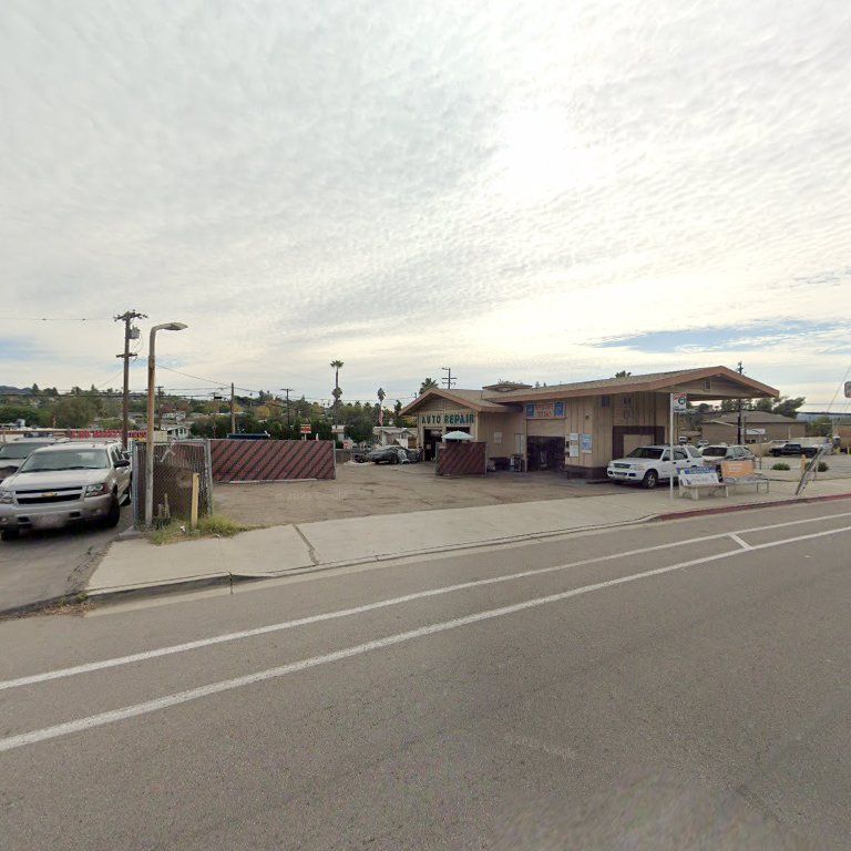 Street view of a small beige building with parked cars and a cloudy sky.
