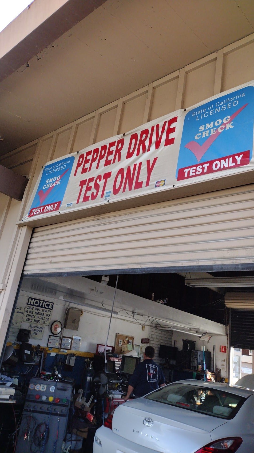Auto shop bay with a red “PEPPER DRIVE TEST ONLY” sign above a partially open garage door.