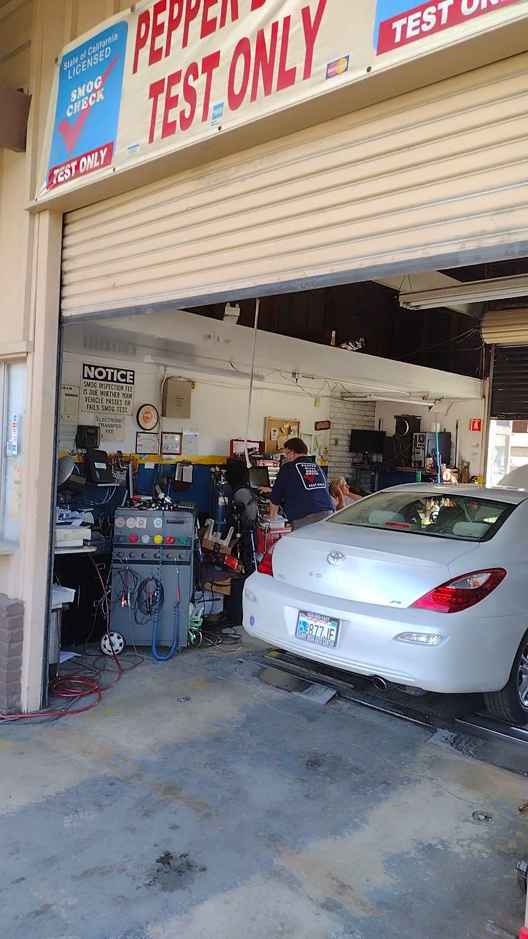 Auto repair garage with a silver sedan parked inside near tools and equipment, roll-up door open