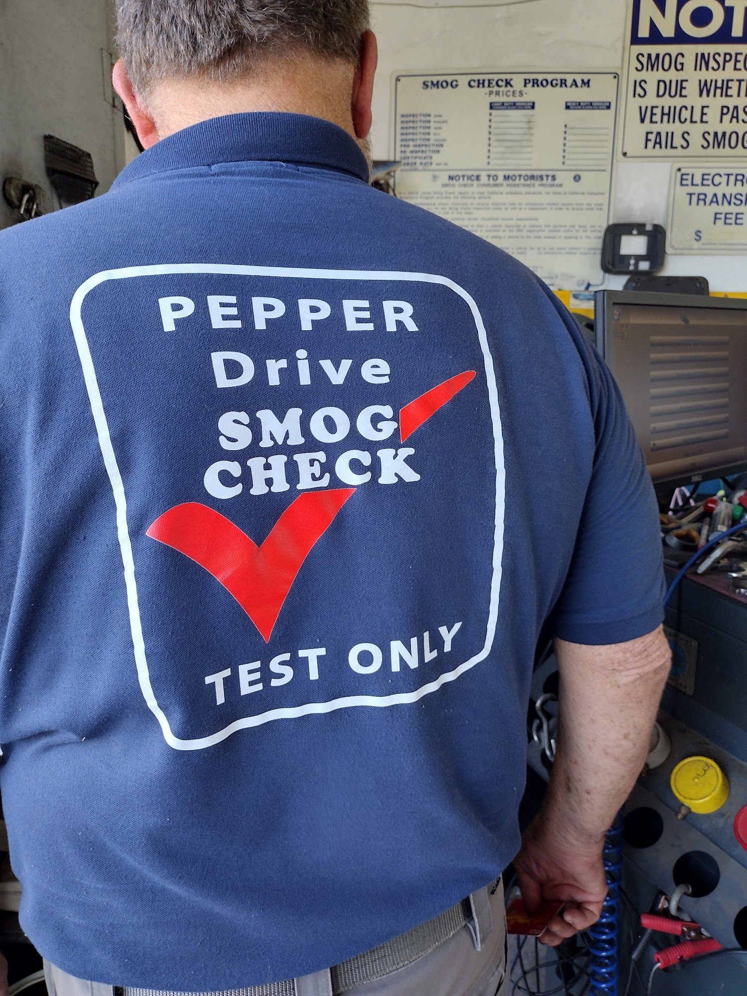 Man in navy shirt with “Pepper Drive Smog Check Test Only” logo, standing at an auto inspection station