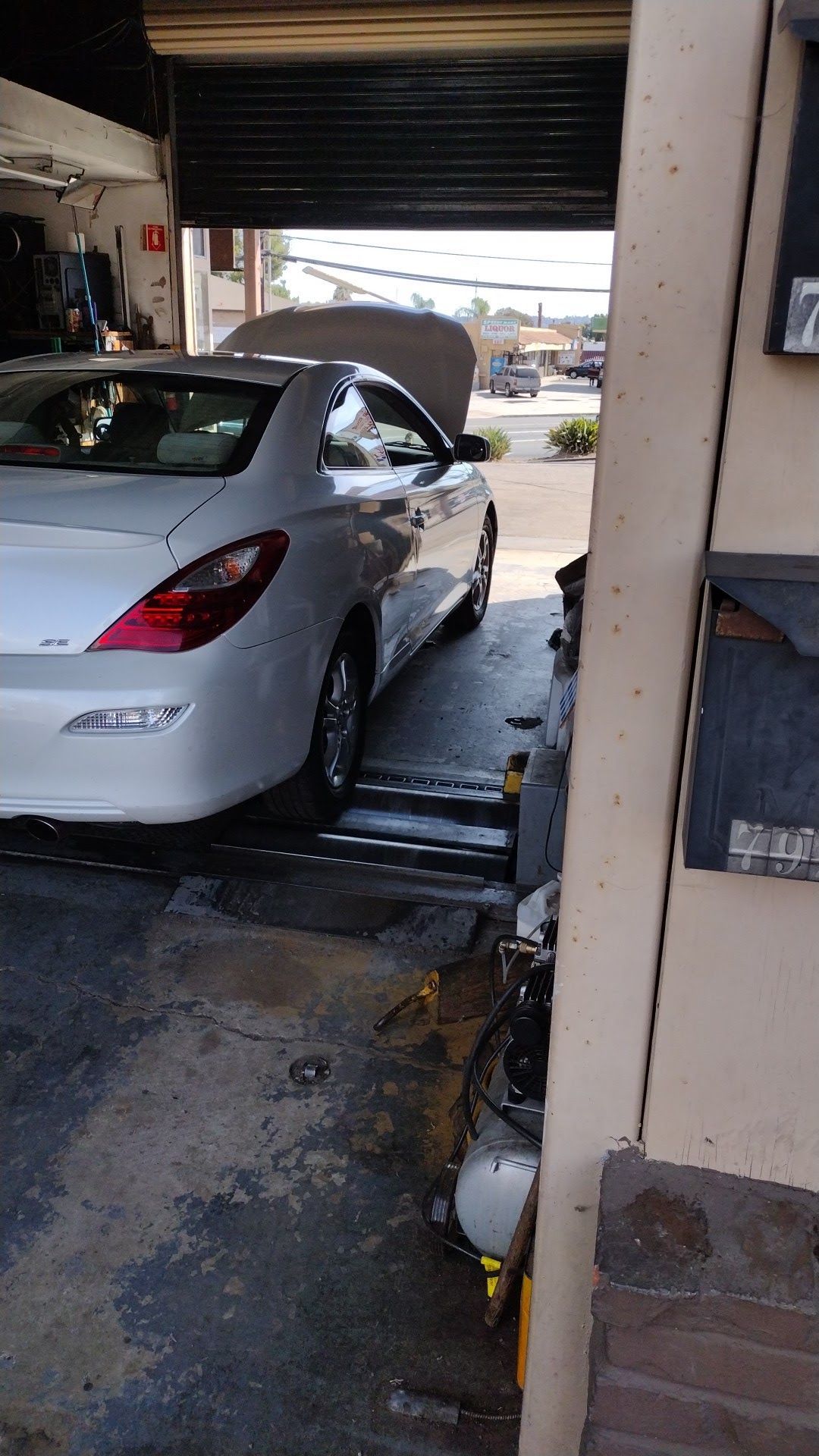 Silver sedan on a car lift inside a garage, viewed from the rear with the trunk open.