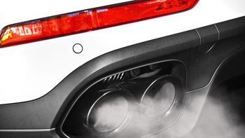 Close-up of a car’s rear bumper and exhaust emitting visible smoke, with a red taillight above.