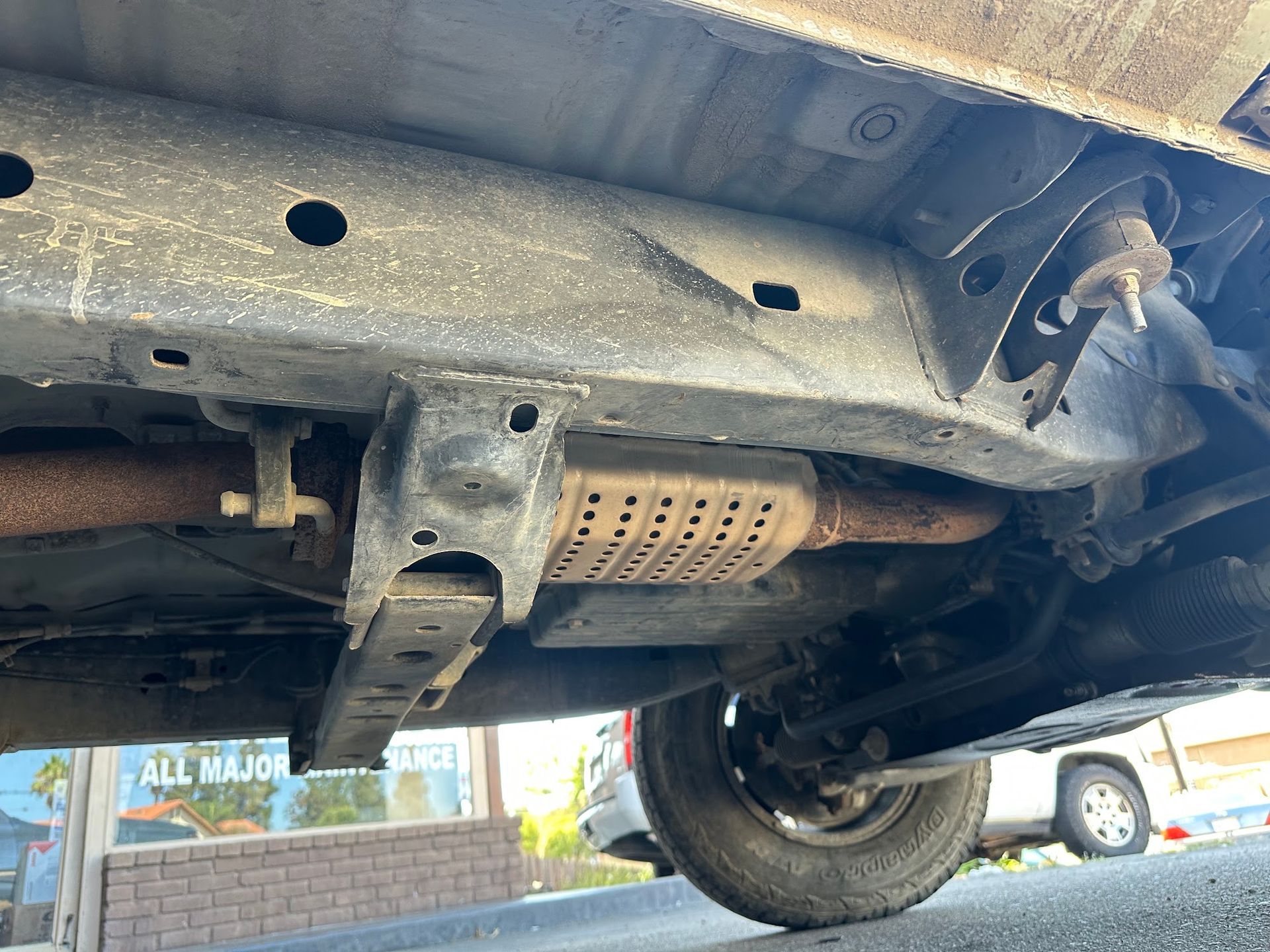 Undercarriage of a vehicle showing exhaust, frame, and rusted components on a lift