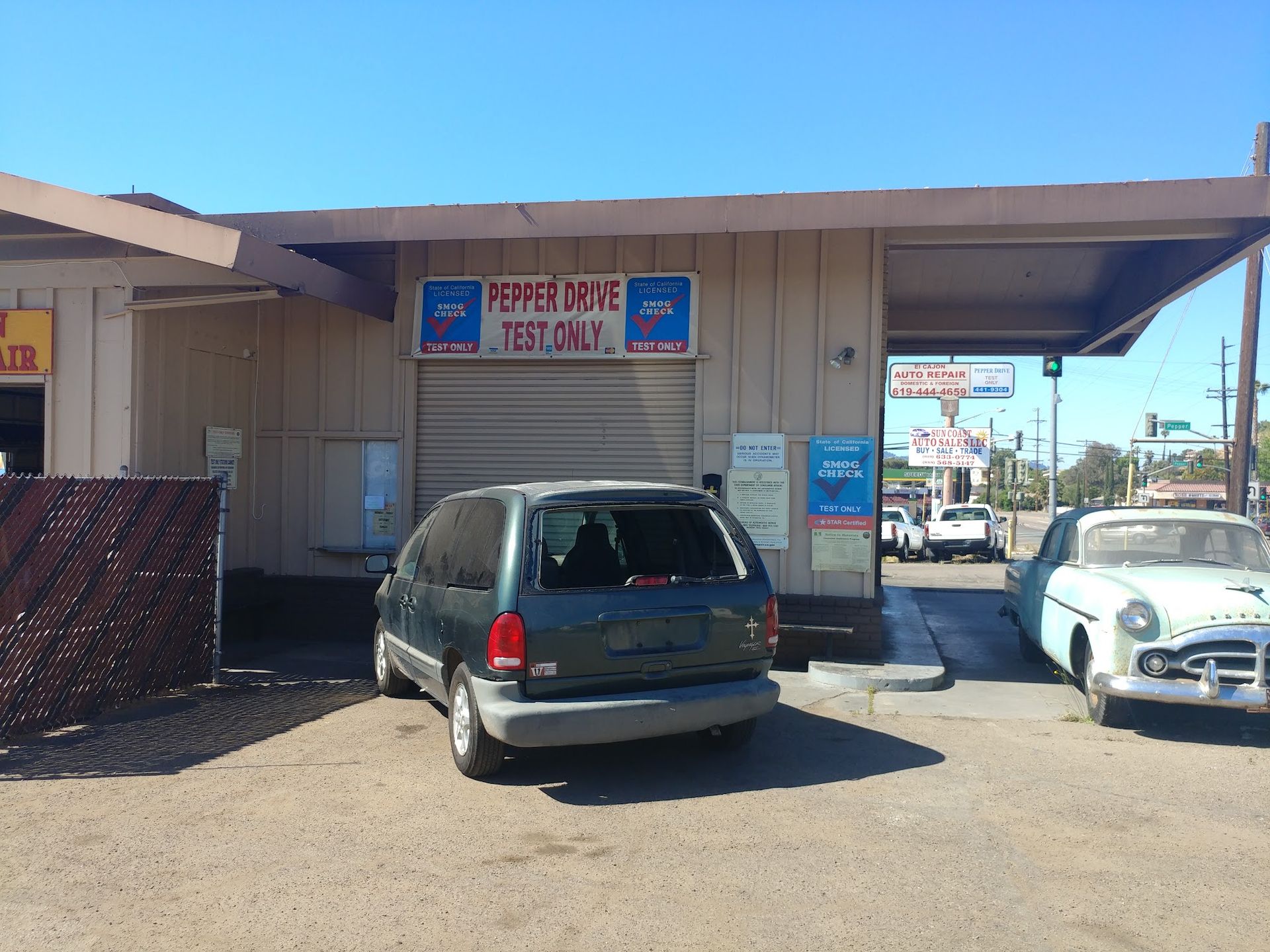 Cars parked outside a small storefront with Japanese signs under a bright blue sky.