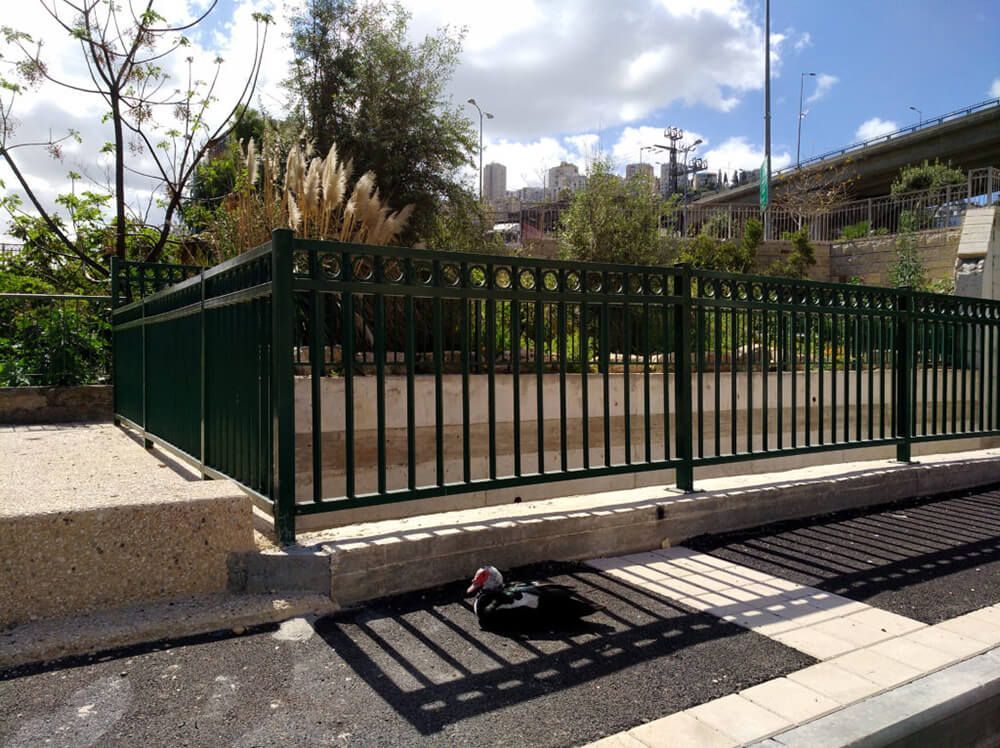 A green fence surrounds a concrete area with trees in the background