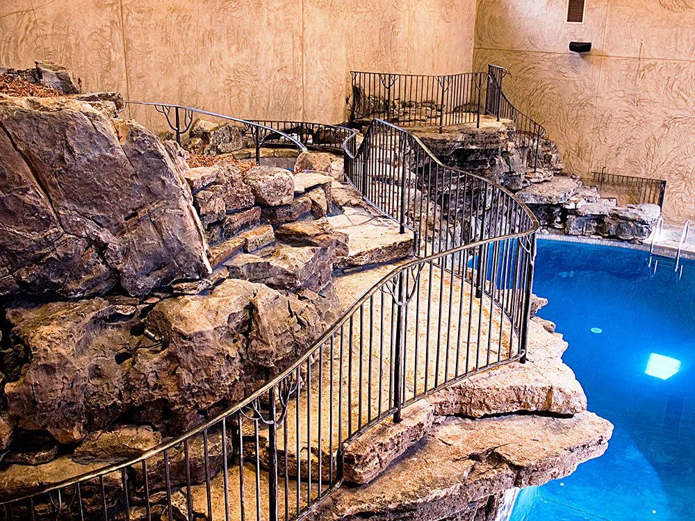 A large swimming pool surrounded by rocks and a metal fence.