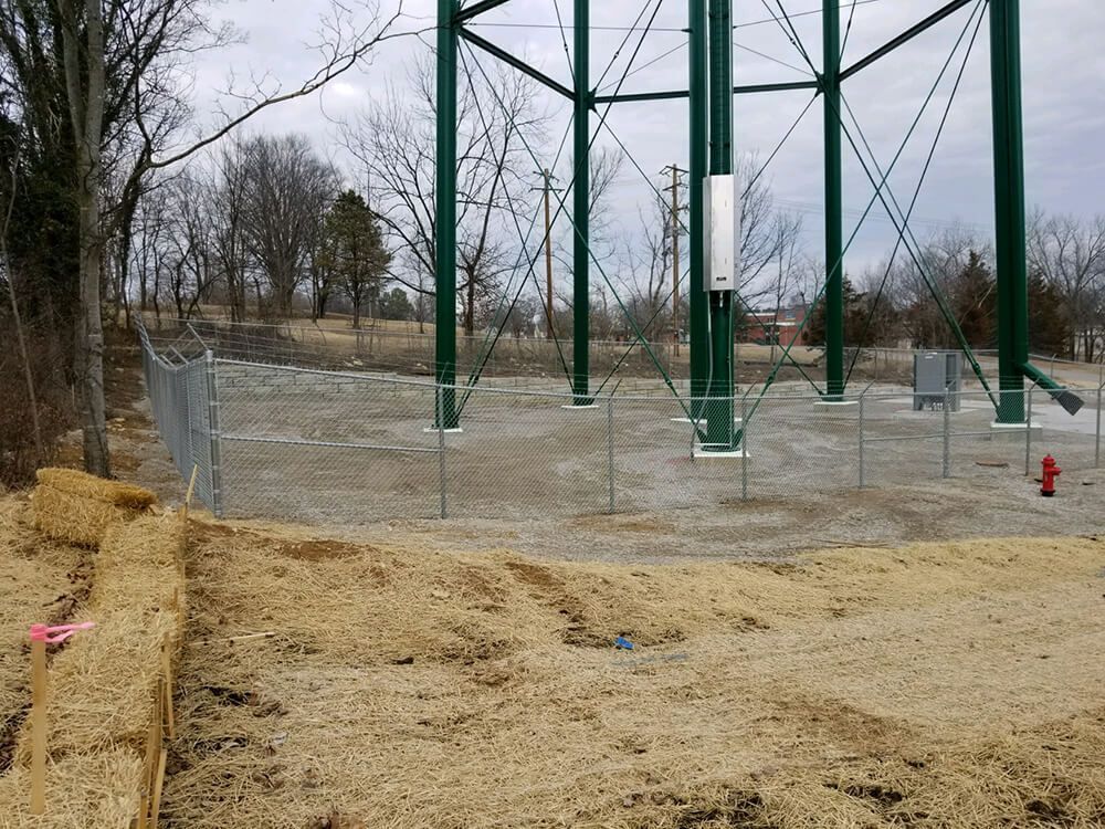 A large green water tower is surrounded by a chain link fence.