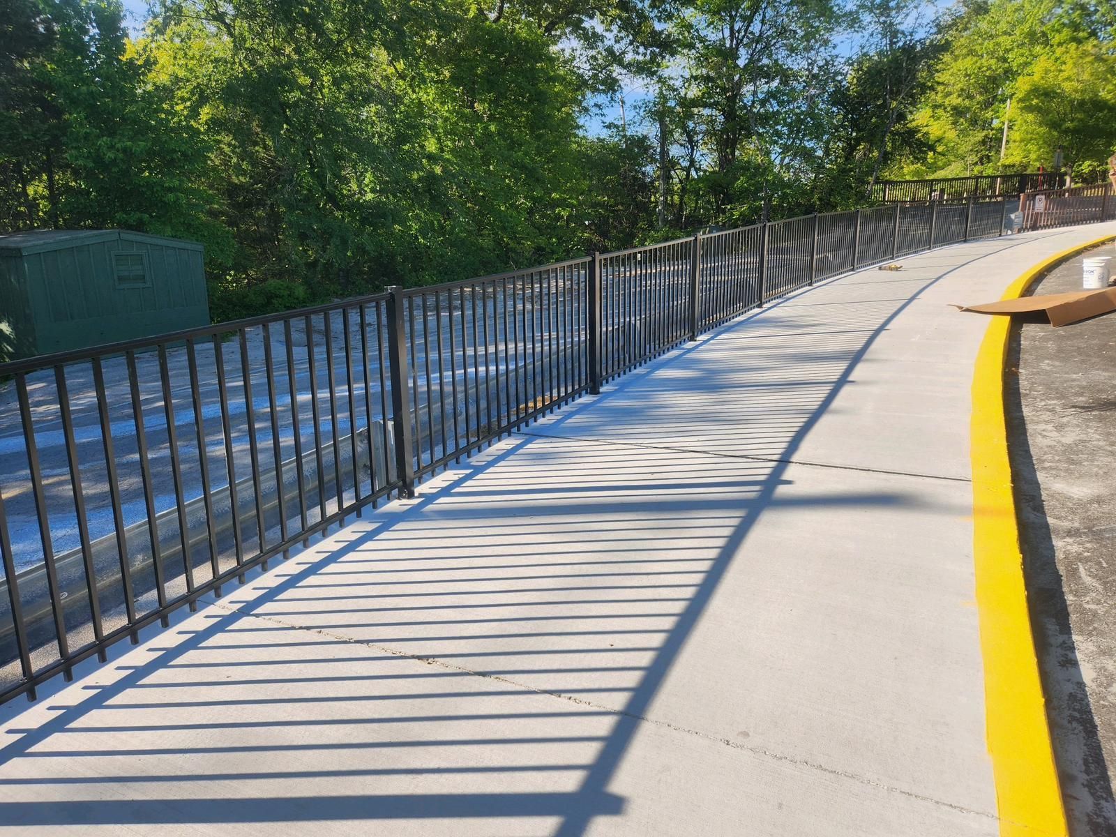 A concrete walkway with a metal fence and a yellow line on the side.