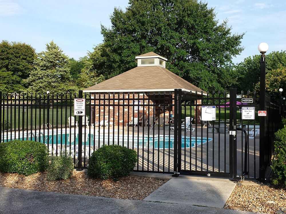 A fence surrounds a swimming pool with a gazebo in the background