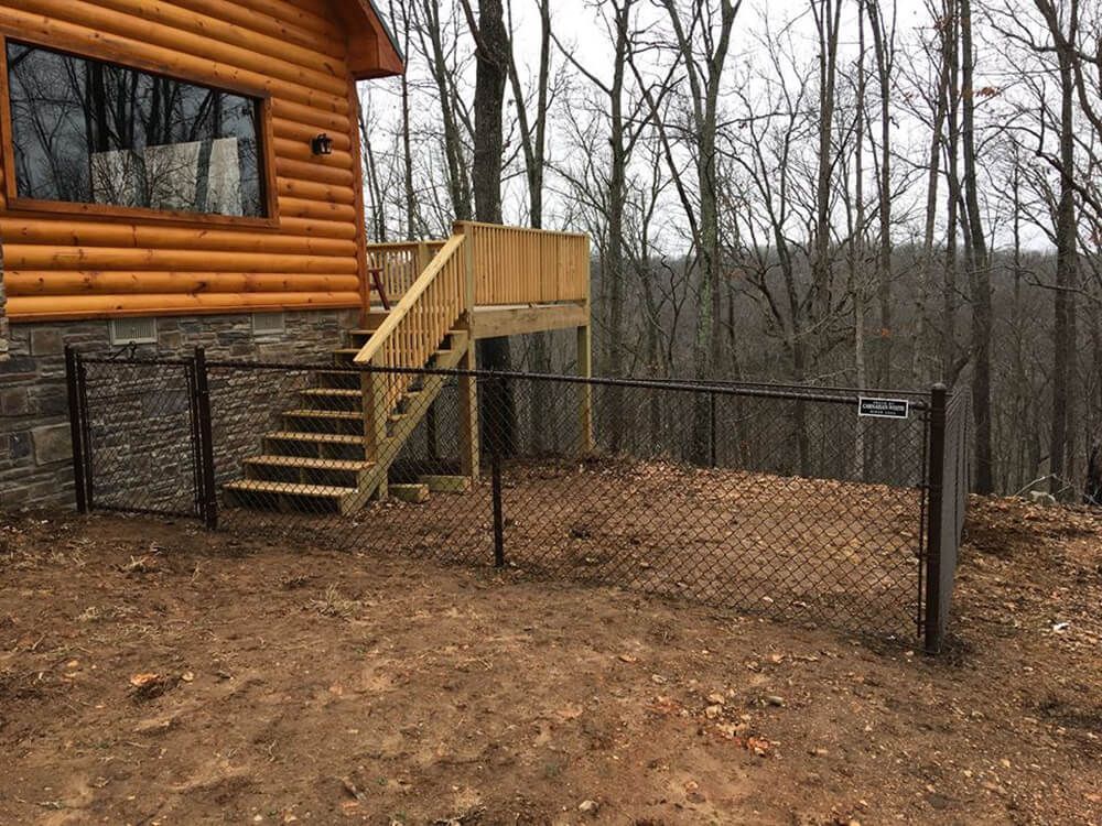 A log cabin with a deck and stairs behind a chain link fence.