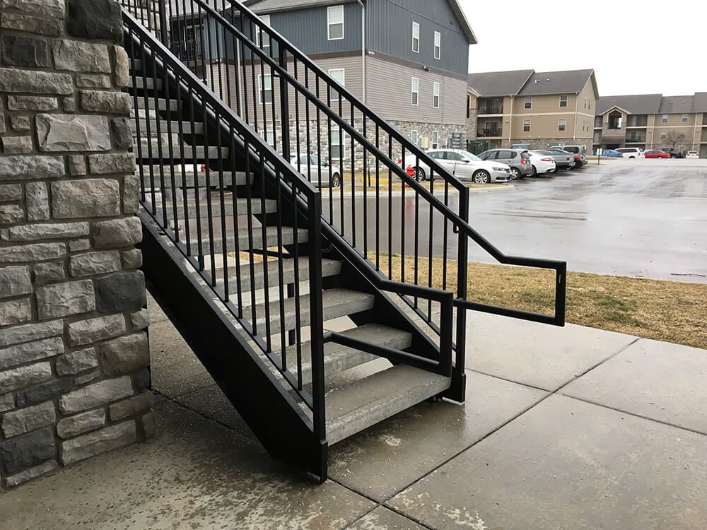 A set of stairs with a metal railing leading up to a parking lot.