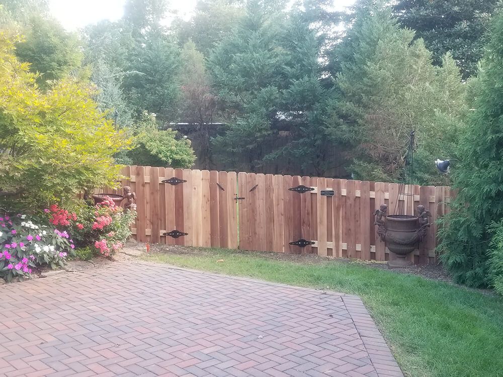 A wooden fence surrounds a brick driveway in a backyard.