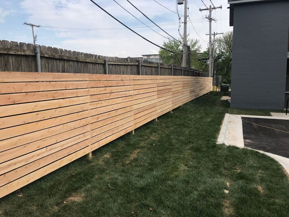 A wooden fence surrounds a lush green yard in front of a building.