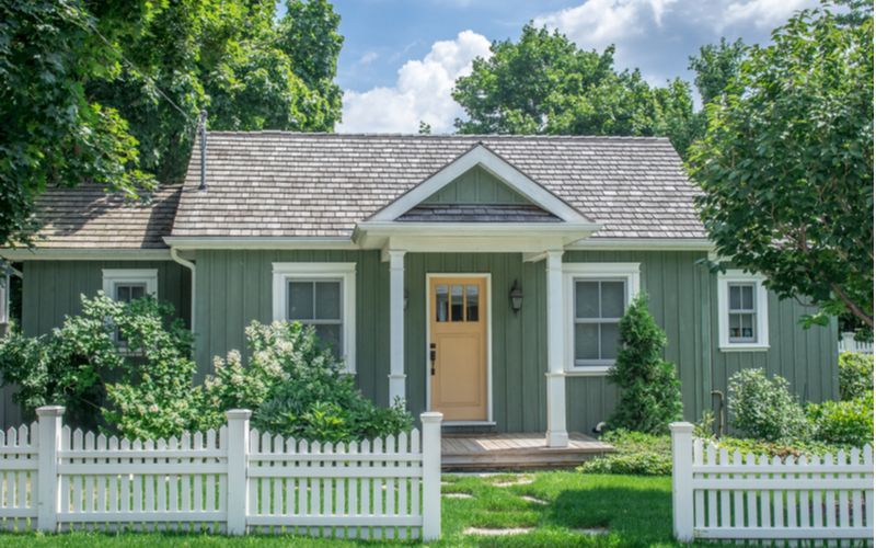 A green house with a white picket fence in front of it.