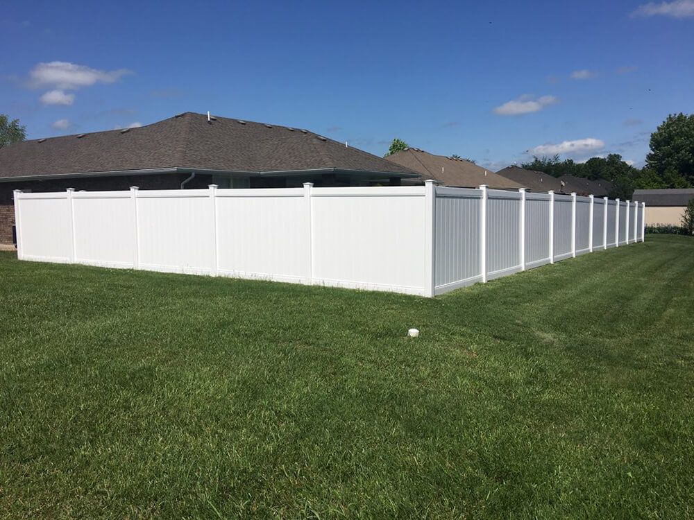 A white vinyl fence surrounds a lush green yard in front of a house.