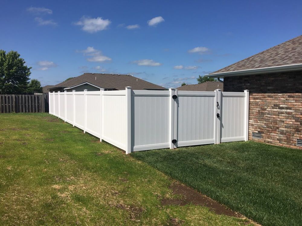 A white fence with a gate in the backyard of a house.