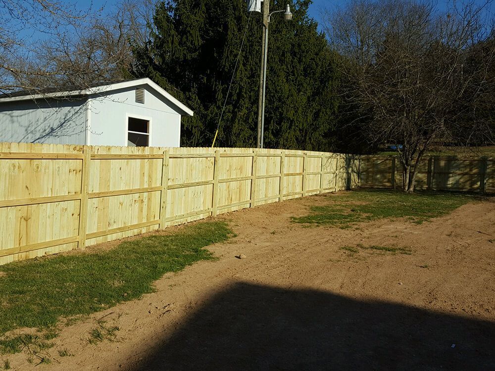 A wooden fence surrounds a grassy area in front of a white shed.
