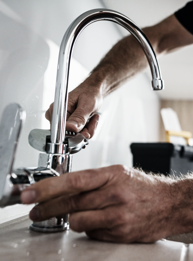 Plumber using a wrench to tighten a faucet in a kitchen.