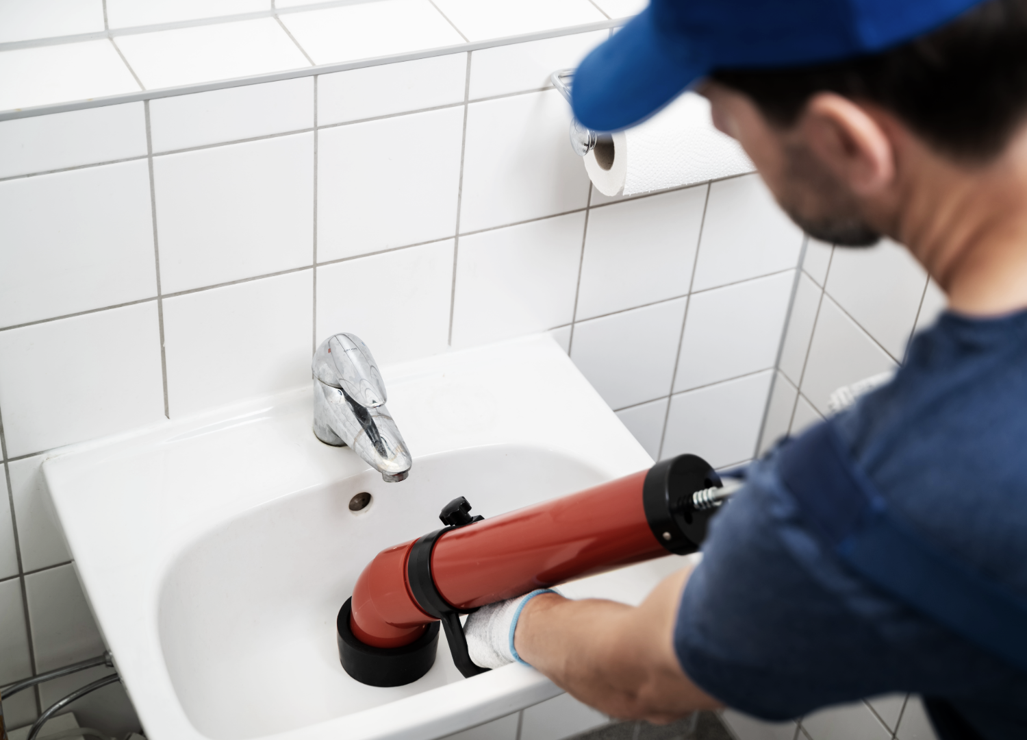Plumber using a plunger to unclog a white sink in a bathroom. 