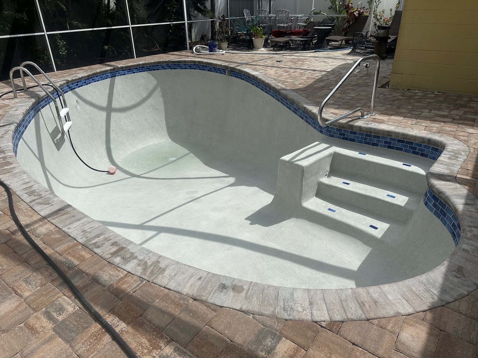 Empty drained backyard swimming pool with built-in steps and blue tile border