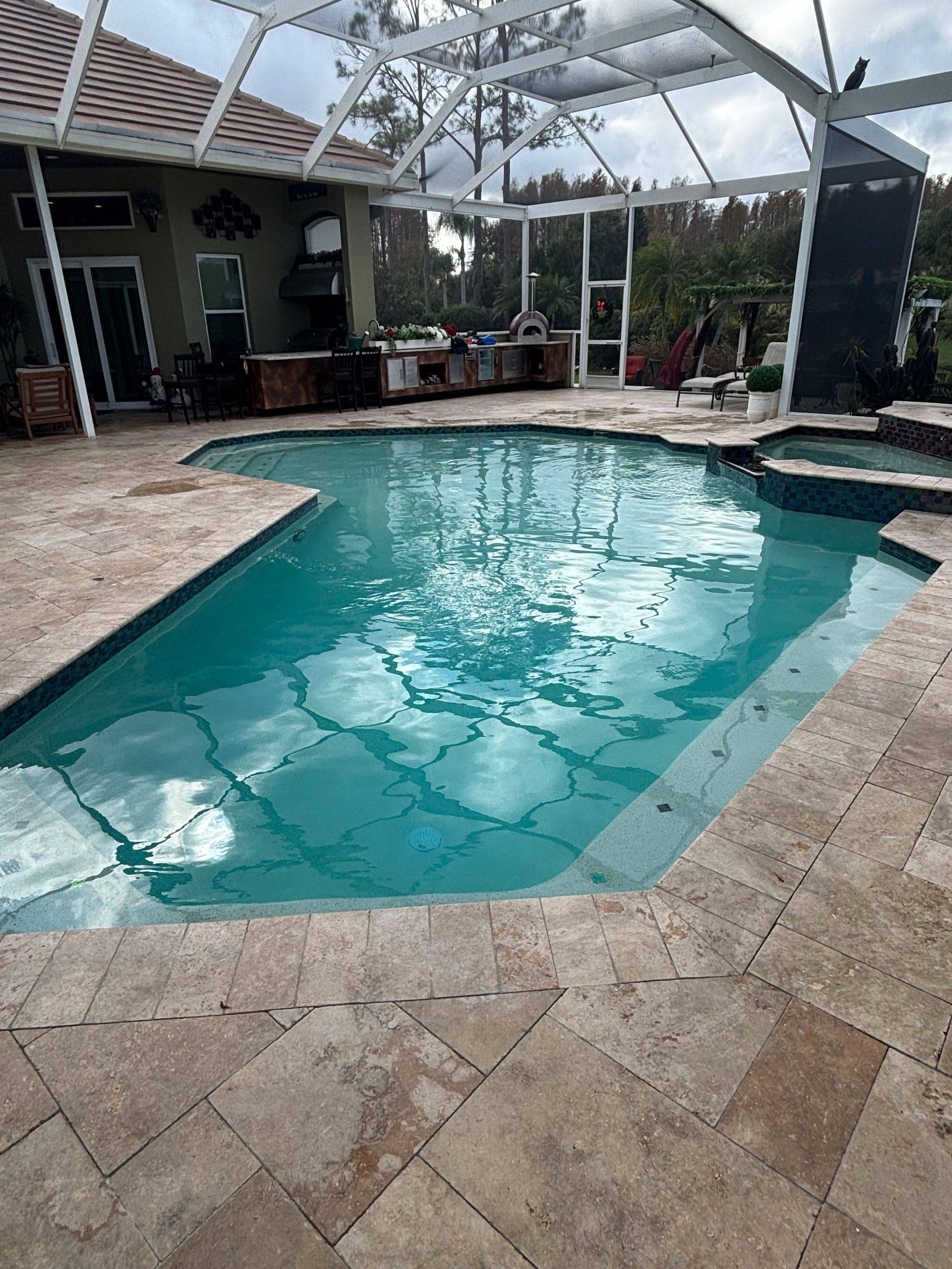 Backyard swimming pool under a screened patio, with tan pavers and a turquoise water surface