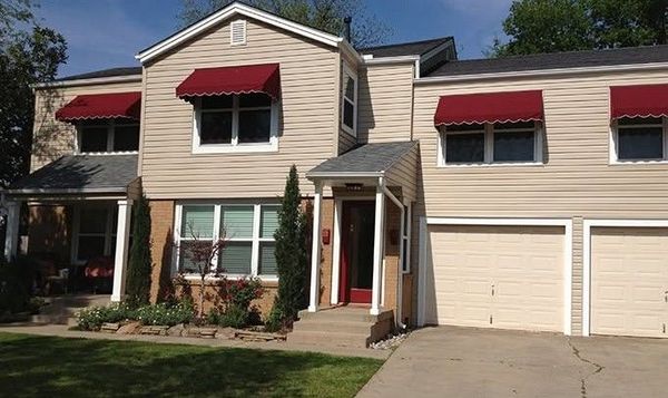 Suburban townhouse with beige siding, red awnings, and an attached double garage on a sunny day