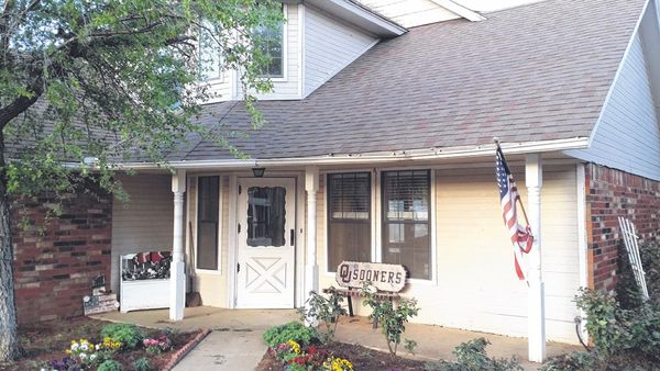 Suburban house porch with brick columns, white trim, flower beds, and an American flag by the door