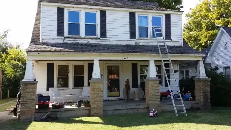 Two-story house with workers on a ladder repairing the upper front roof area
