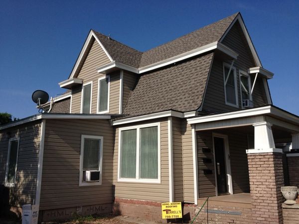 Two-story house with brown siding, steep roof, and a small front porch under a clear blue sky
