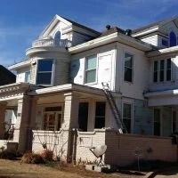 White two-story house with a front porch and ladder leaning against the side under a blue sky