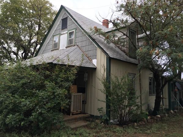 Old weathered house with a steep roof, overgrown vines, and trees surrounding it