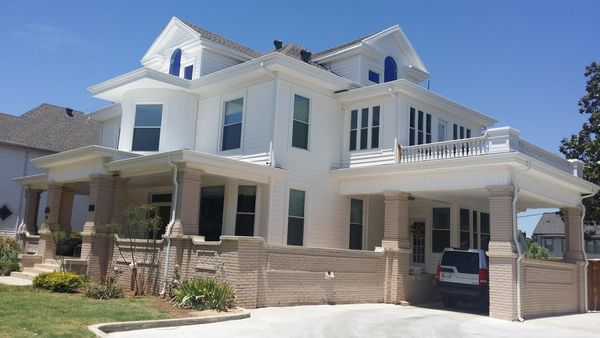 Large white two-story house with a stone facade, covered porch, and driveway under a bright blue sky