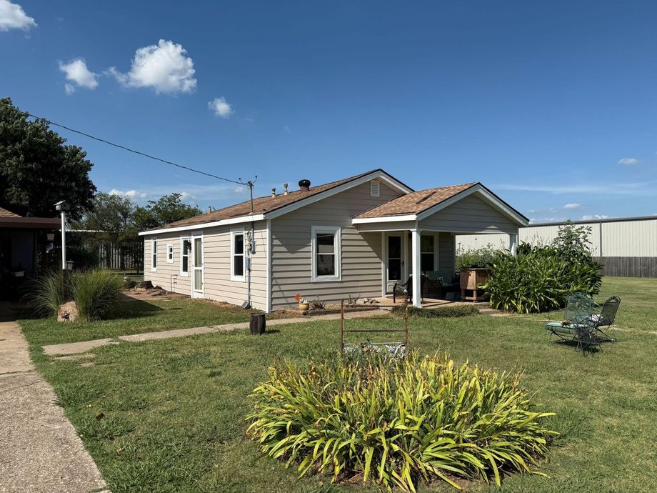 Single-story beige house with a porch and garden under a clear blue sky