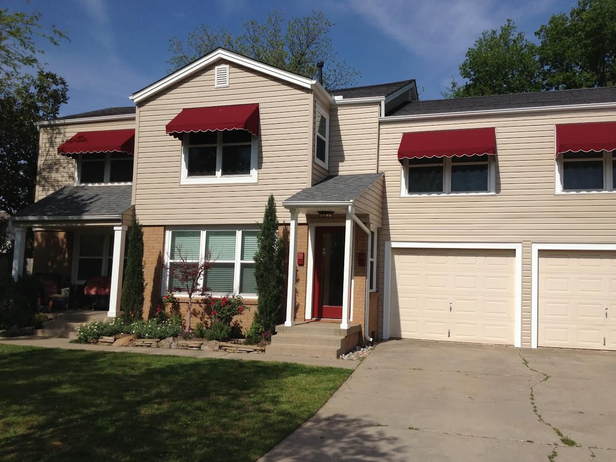 Two-story beige house with red awnings, front lawn, and driveway with a double garage.