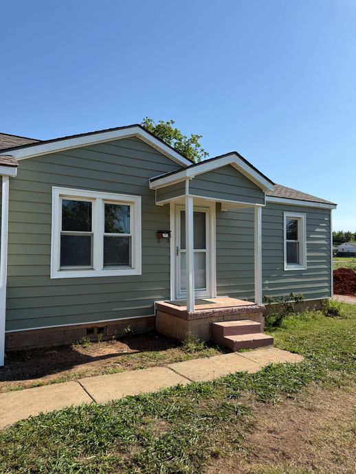Small gray house with white trim, front steps, and a sunny yard under a blue sky