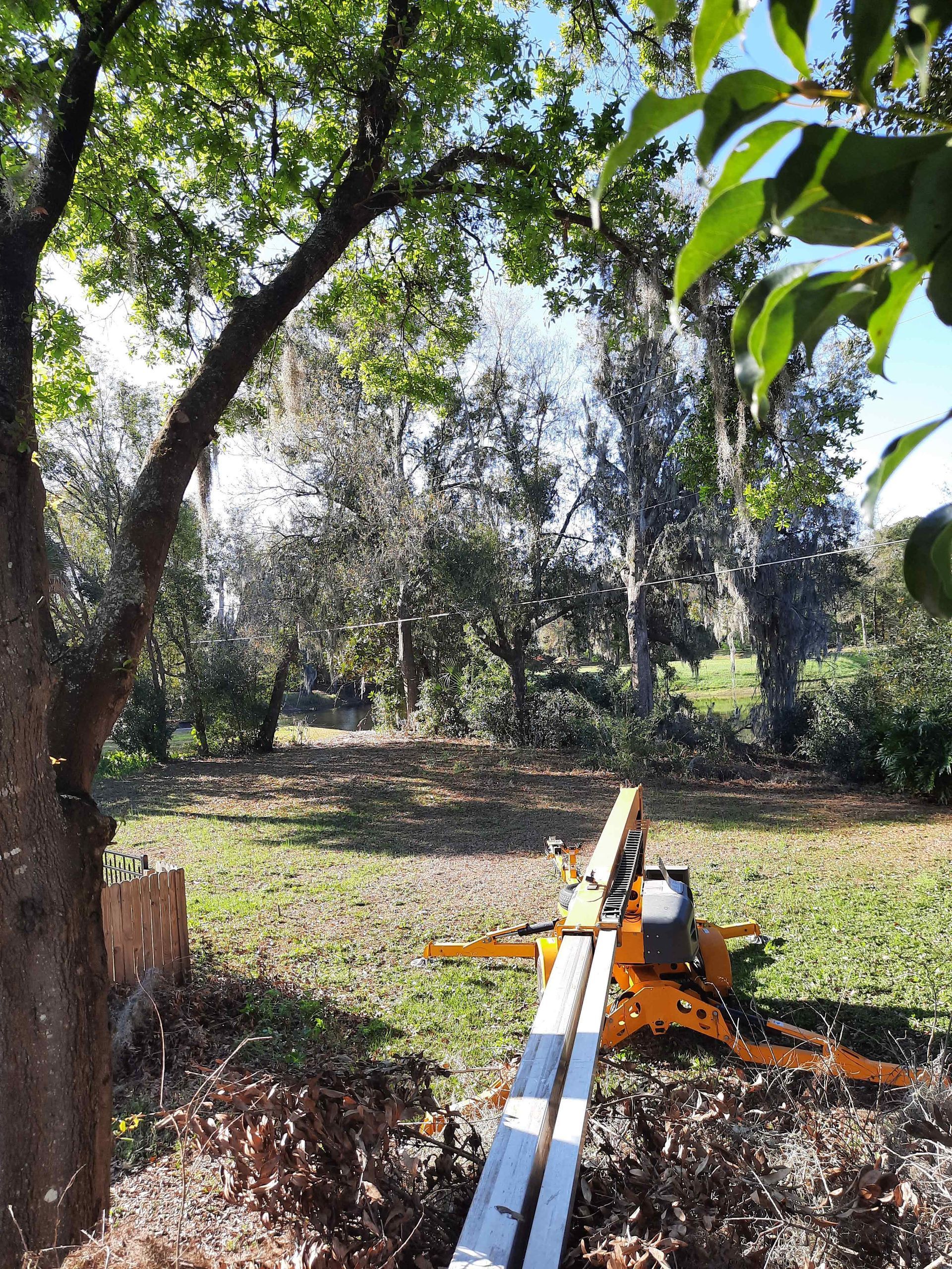 A bright orange lift is set up in a yard, under trees with green foliage.