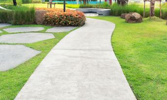 Curved concrete garden path bordered by green lawn, stepping stones, and shrubs leading to a pond