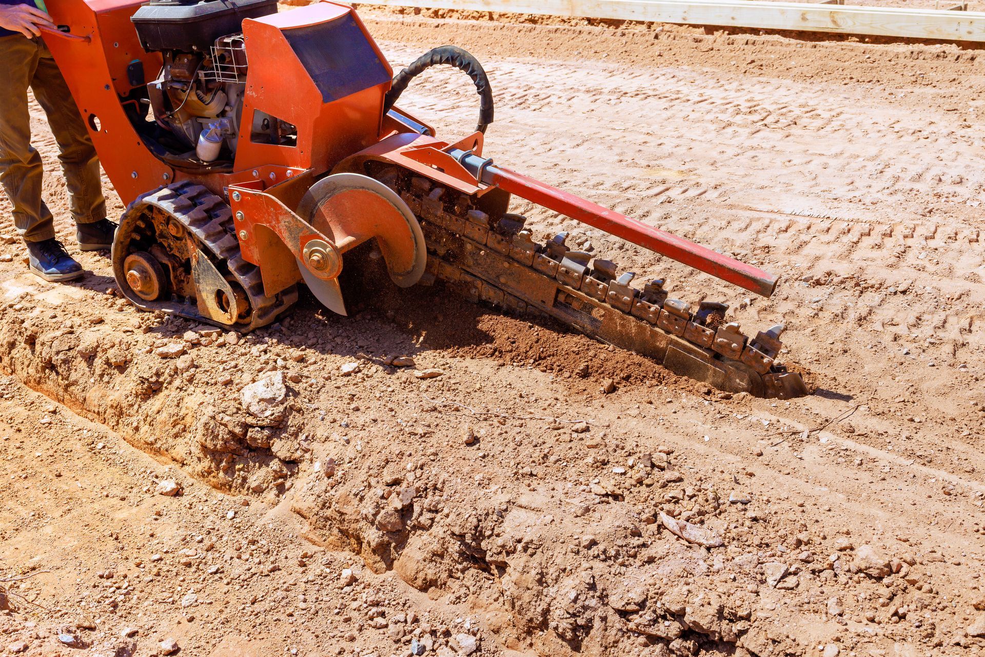 Tracked trenching machine digging a narrow trench in dry soil outdoors.