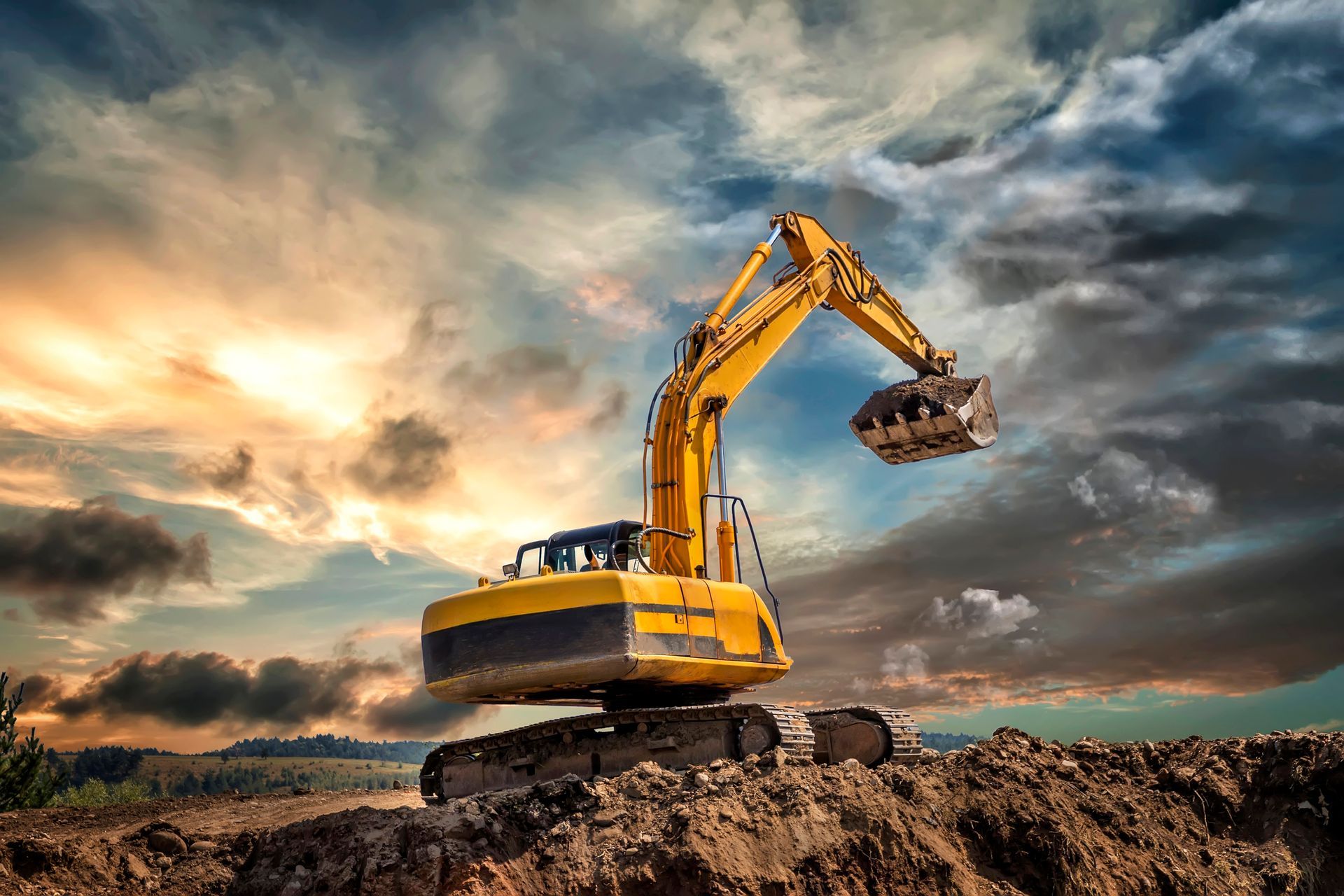 Yellow excavator against a dramatic sunset sky, scooping earth from a dirt mound.