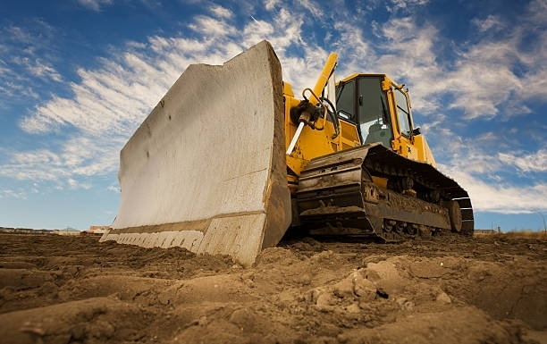 Yellow bulldozer with large blade grading dirt at construction site under blue sky.