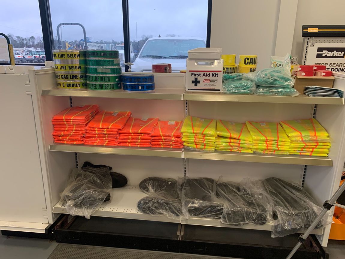 Shelves stocked with safety gear, including vests, tape, a first aid kit, and gloves.
