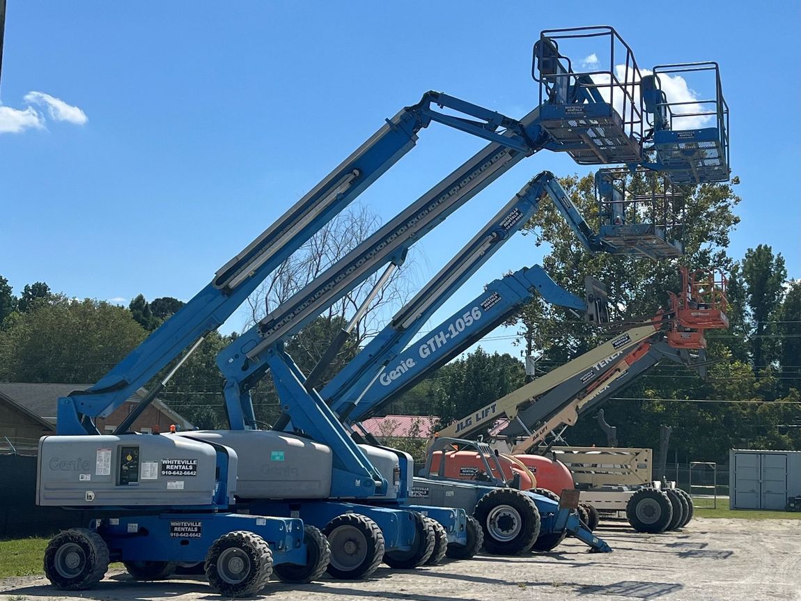 Blue and orange boom lifts parked outdoors under a sunny sky.