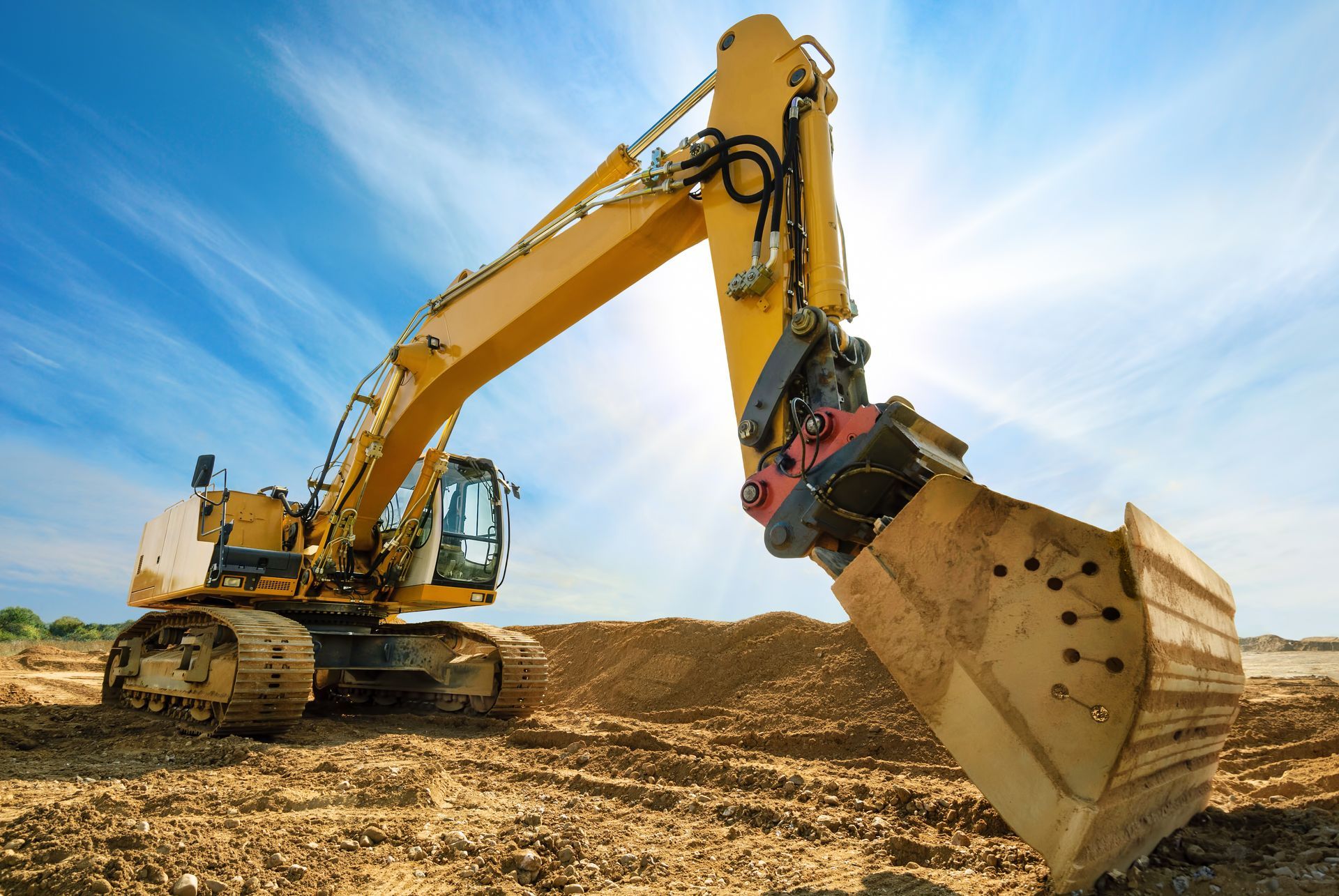 Yellow excavator on a construction site, digging in the dirt under a bright blue sky.