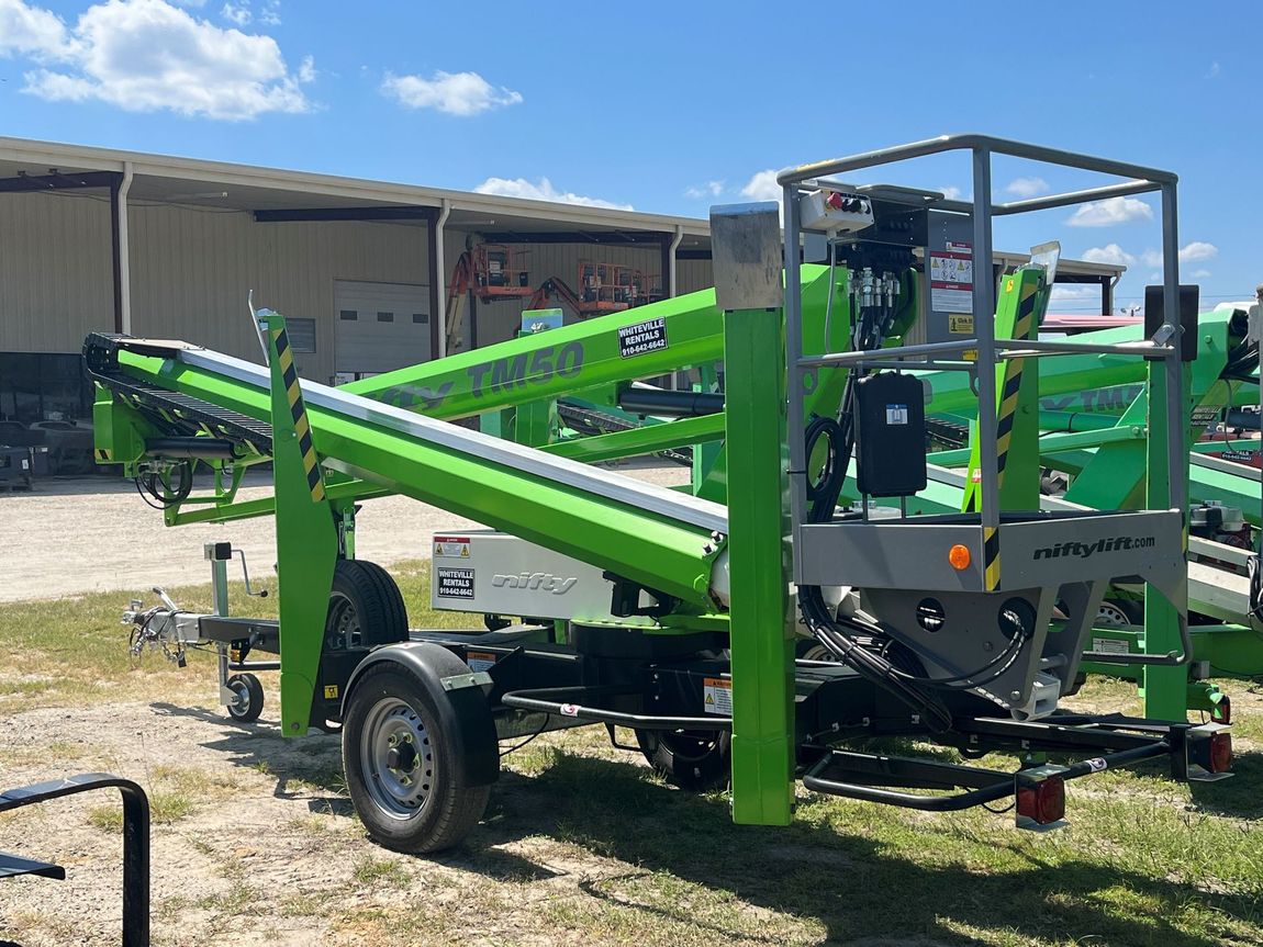 Green and black aerial lift on a trailer outdoors under a blue sky.