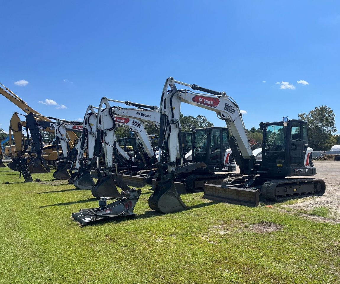 Several white and black Bobcat excavators parked on grass under a blue sky.