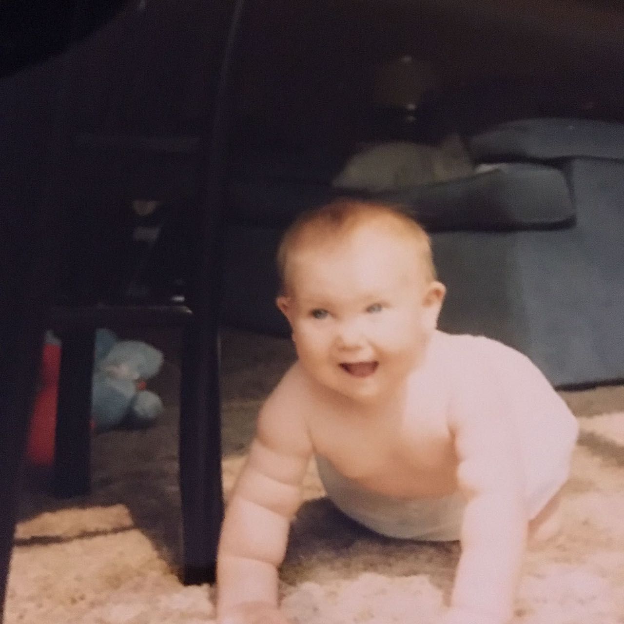 Smiling baby crawls on a carpet, under a table.
