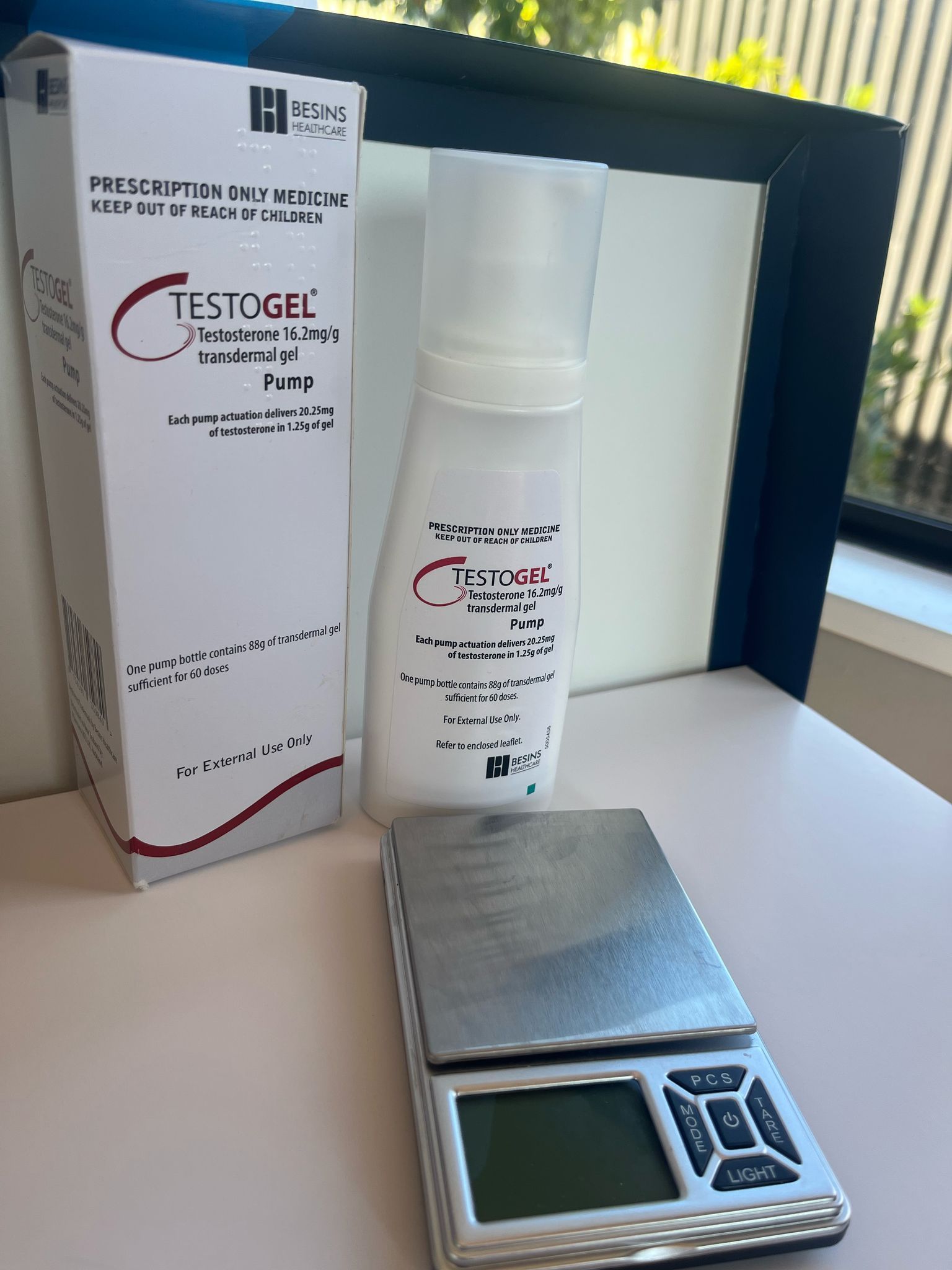A bottle of Testogel, a box, and a digital scale are on a white surface.