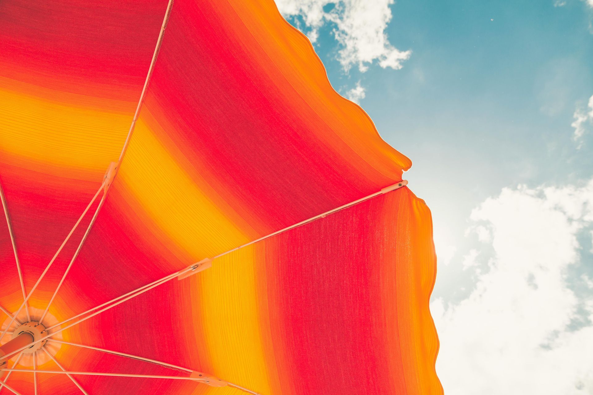 Red and yellow striped beach umbrella against a blue sky with white clouds.